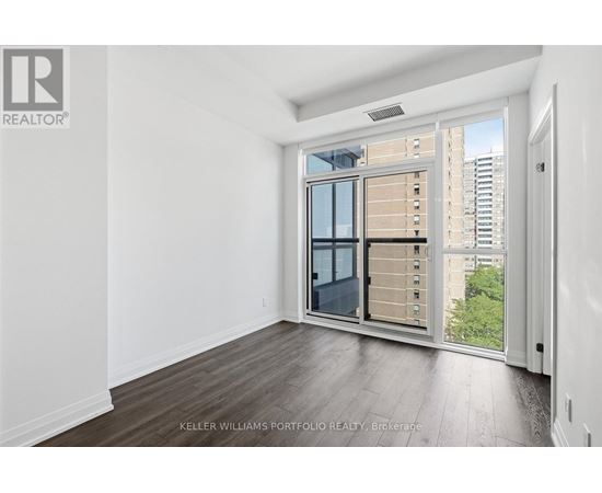 A real estate listing image of a room with a large window and a view of a city.