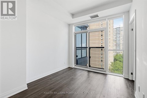 A real estate listing image of a room with a large window and a view of a city.