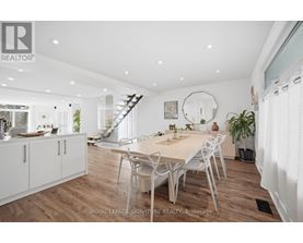 A dining room with a table and chairs in the foreground and a staircase in the background.