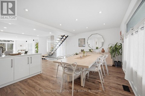A dining room with a table and chairs in the foreground and a staircase in the background.