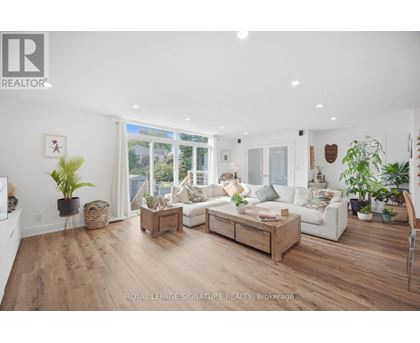 A well-lit, spacious living room with a white sofa set and wooden flooring.