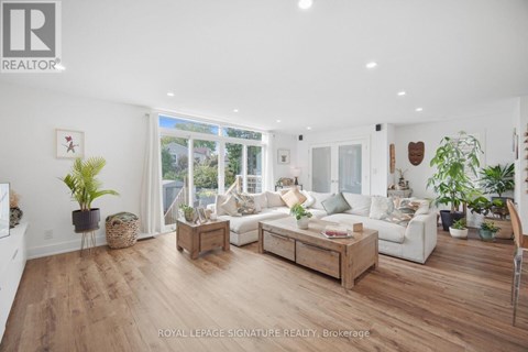 A well-lit, spacious living room with a white sofa set and wooden flooring.