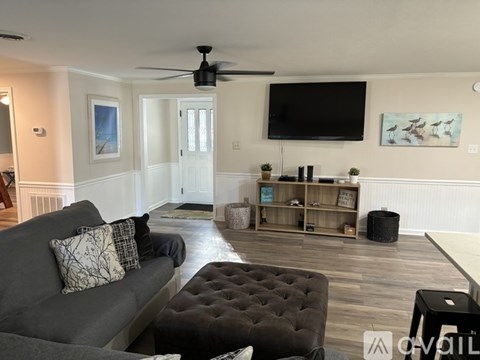 A living room with a grey couch and a black tufted ottoman.