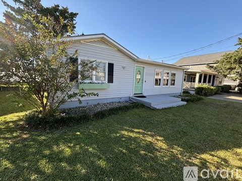A house with a green door and white siding is surrounded by a grassy lawn.