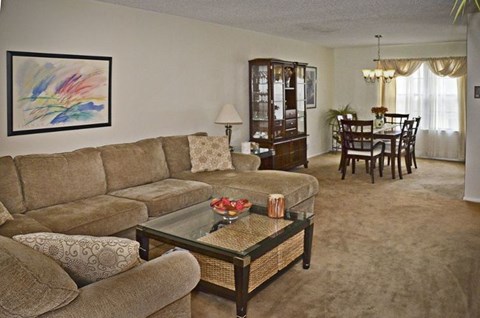 A living room with a glass coffee table and a painting on the wall.