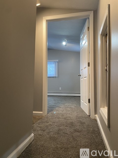 A hallway with a carpeted floor and white walls leading to a bedroom.