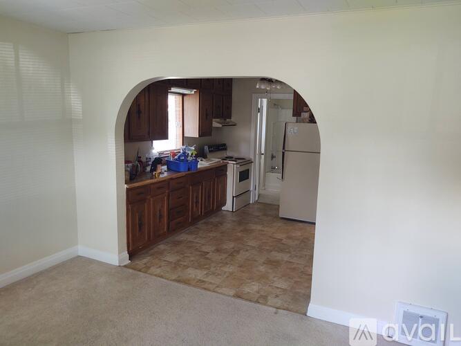 A kitchen with a refrigerator, sink, and cabinets is visible through an archway.