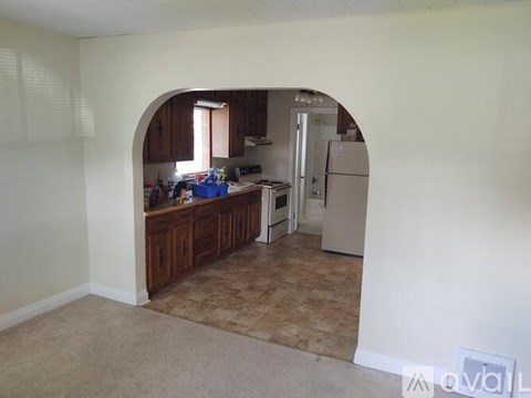 A kitchen with a refrigerator, sink, and cabinets is visible through an archway.