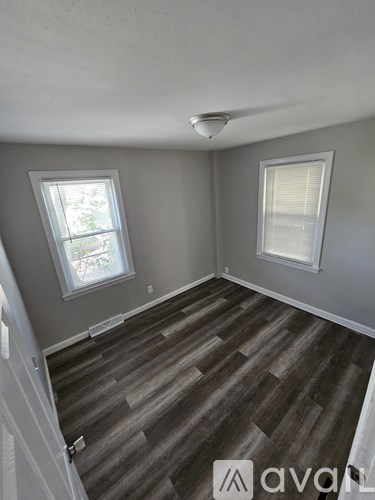 A room with wooden flooring and two windows.