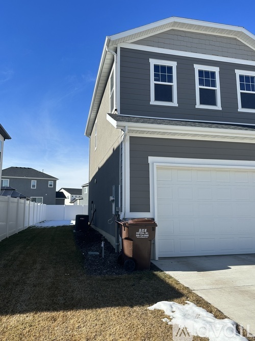 A house with a grey and white exterior and a brown trash can in front of it.