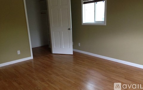 A room with a white door and a window with wooden flooring.