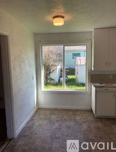 A room with a window showing a view of a fence and a building outside.