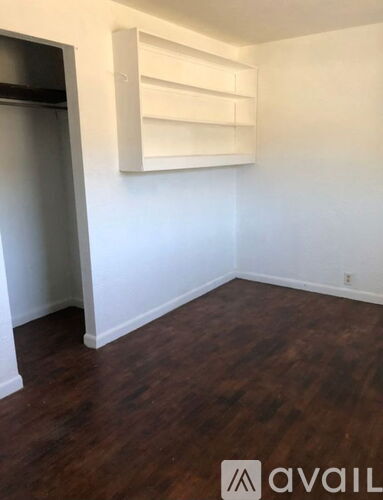 A room with wooden floors and a white wall with a shelf on it.