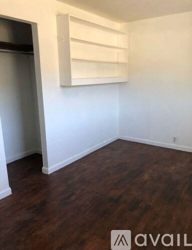A room with wooden floors and a white wall with a shelf on it.