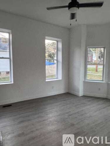 A room with a ceiling fan and two windows.