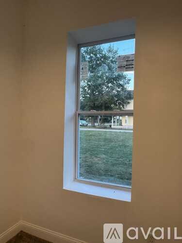 A window with a view of a green lawn and buildings outside.