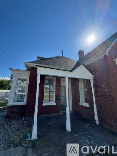 A small red brick house with a porch and a sun shining in the background.