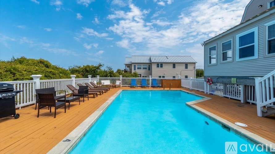 A pool with a deck and chairs in front of a house.