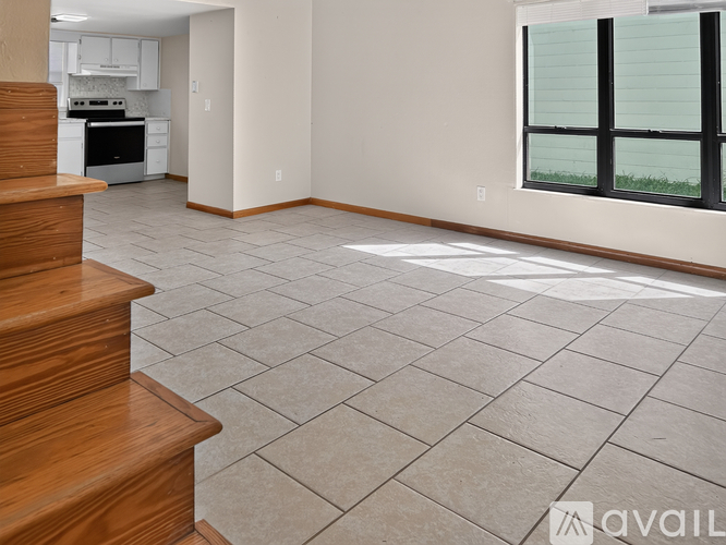 A living room with a kitchen in the background and a staircase on the left.