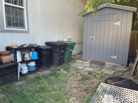 A shed is next to a green barrel and a black dumpster.