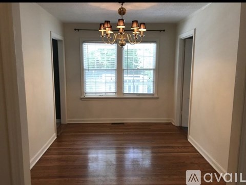 A room with a chandelier and a window with blinds.
