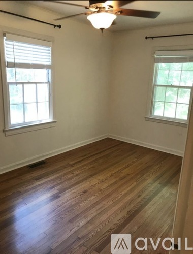 A room with wooden flooring and two windows.