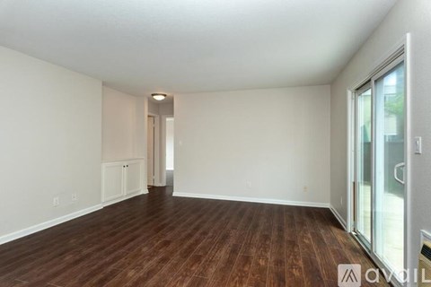 A spacious room with wooden flooring and white walls.