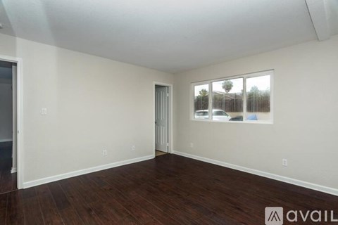 A room with wooden floors and white walls, with a window showing a view of a fence and trees.
