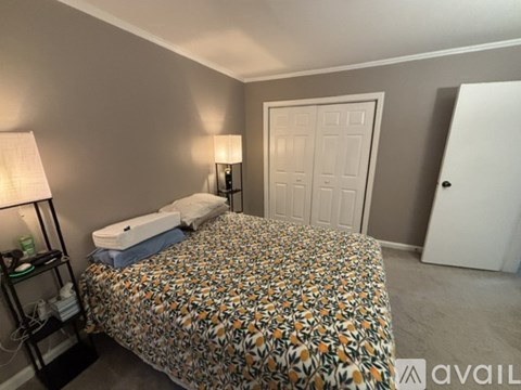 A bedroom with a bed covered in a floral print bedspread, a white pillow, a lamp on a side table, and two doors.