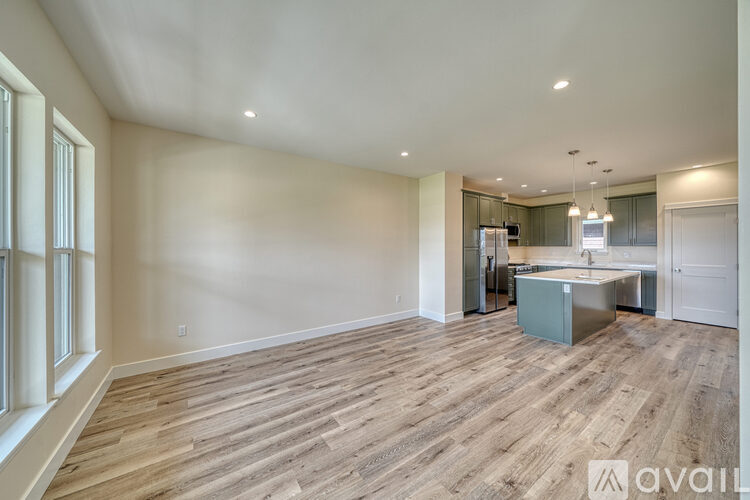A spacious room with wooden flooring and a kitchen area in the background.