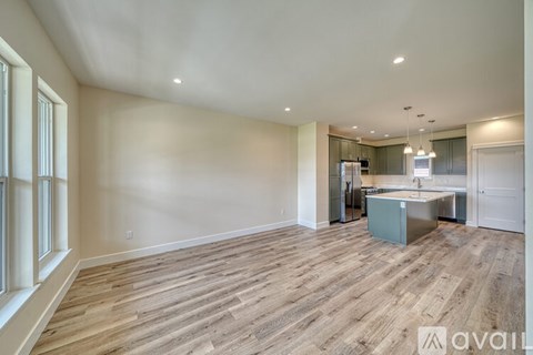 A spacious room with wooden flooring and a kitchen area in the background.