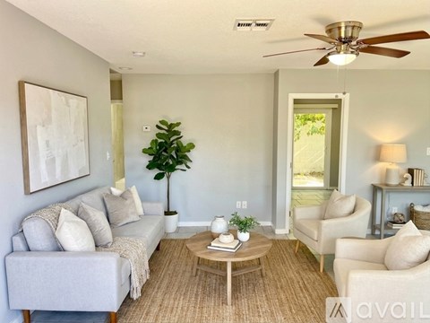 A living room with a grey couch, a coffee table, a ceiling fan, and a painting on the wall.