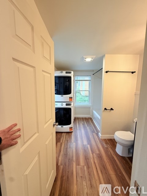 A person is opening a white door to a room with a toilet and a washing machine.