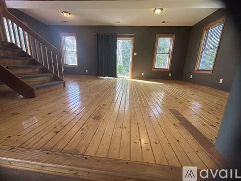 A spacious room with wooden flooring and a staircase on the left side.