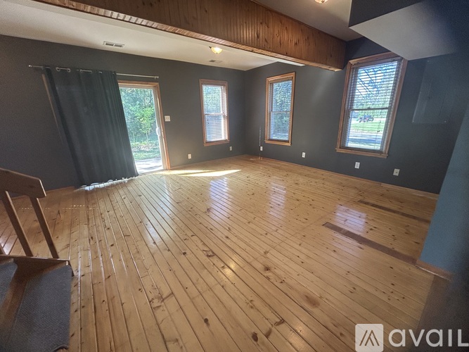 A room with wooden flooring and a window with a view of trees.