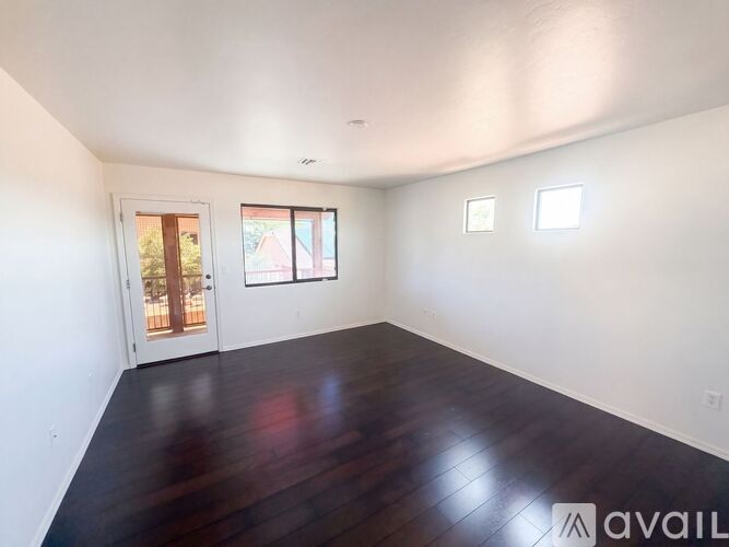 A room with wooden floors and white walls, with a door and two windows.