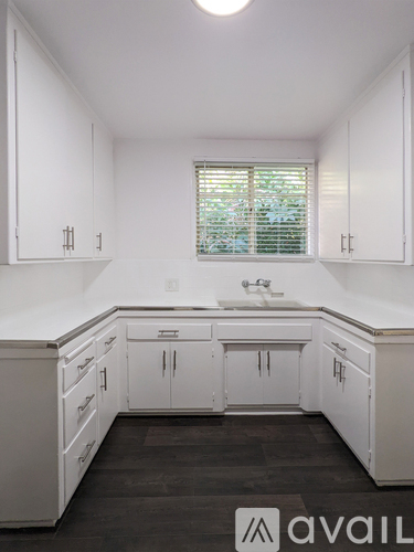 A kitchen with white cabinets and a window with blinds.