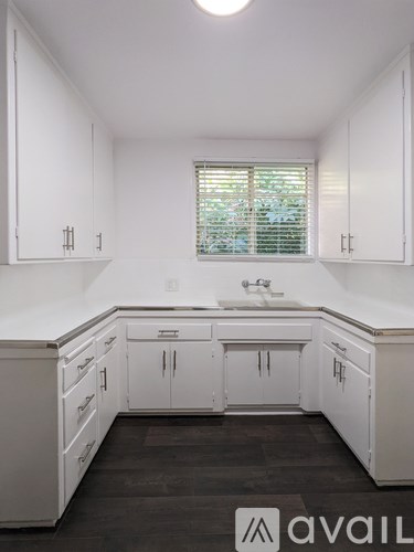 A kitchen with white cabinets and a window with blinds.