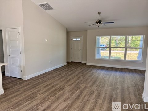 A room with a ceiling fan and a window with a view of a car and trees outside.