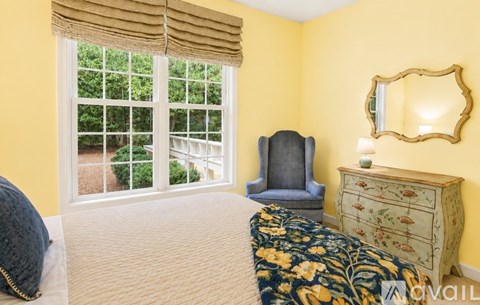 A bedroom with a bed, a chair, and a dresser with a mirror.