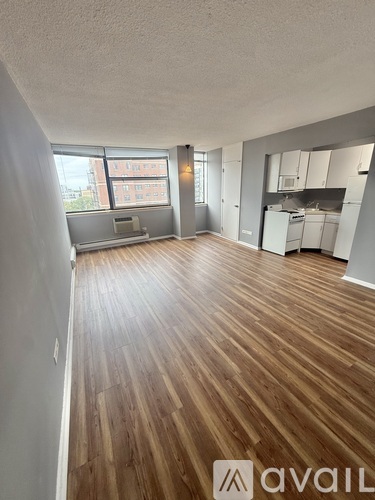 A spacious room with wooden flooring and a kitchen area in the background.