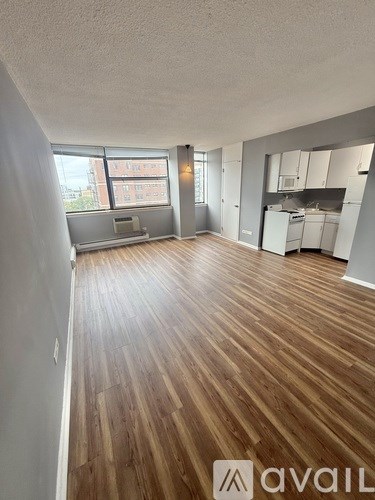 A spacious room with wooden flooring and a kitchen area in the background.