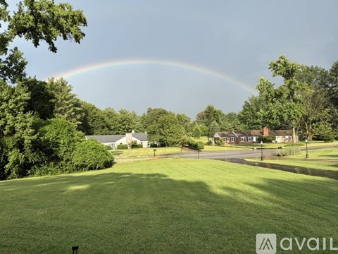 A rainbow appears over a green field with houses in the background.