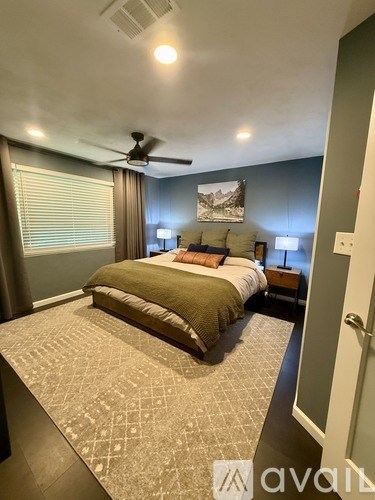 A bedroom with a bed, a ceiling fan, and a painting on the wall.