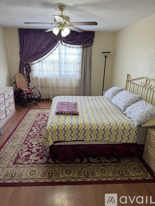 A bedroom with a bed, chair, and window with curtains.
