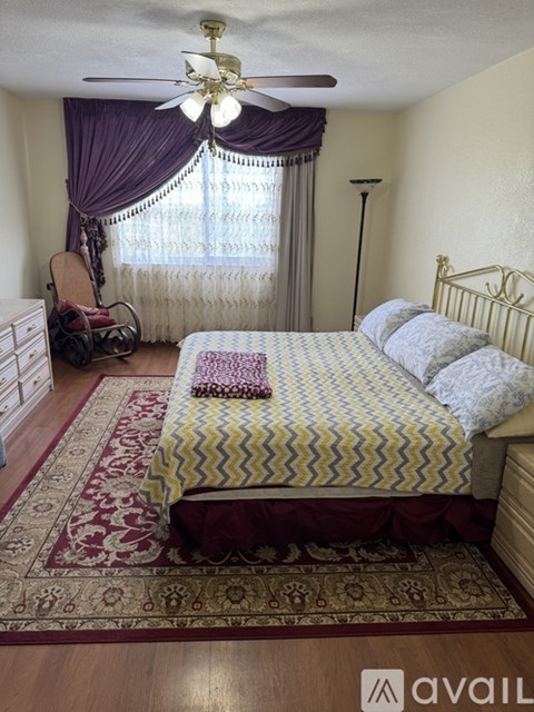 A bedroom with a bed, chair, and window with curtains.