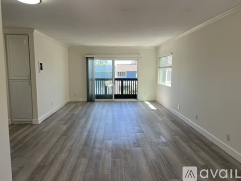 A spacious room with wooden flooring and a balcony with a railing.