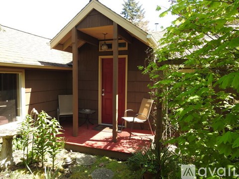 A small wooden cabin with a red door is surrounded by greenery.