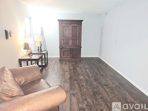 A living room with a brown leather couch, a wooden cabinet, and a wooden floor.