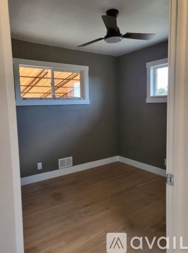 A room with a ceiling fan and two windows.